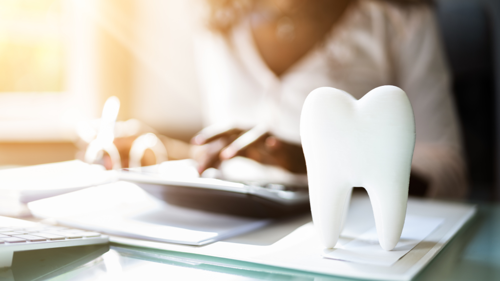 Tooth model on desk with paperwork and dentist in background, representing dental treatment planning and insurance consultation
