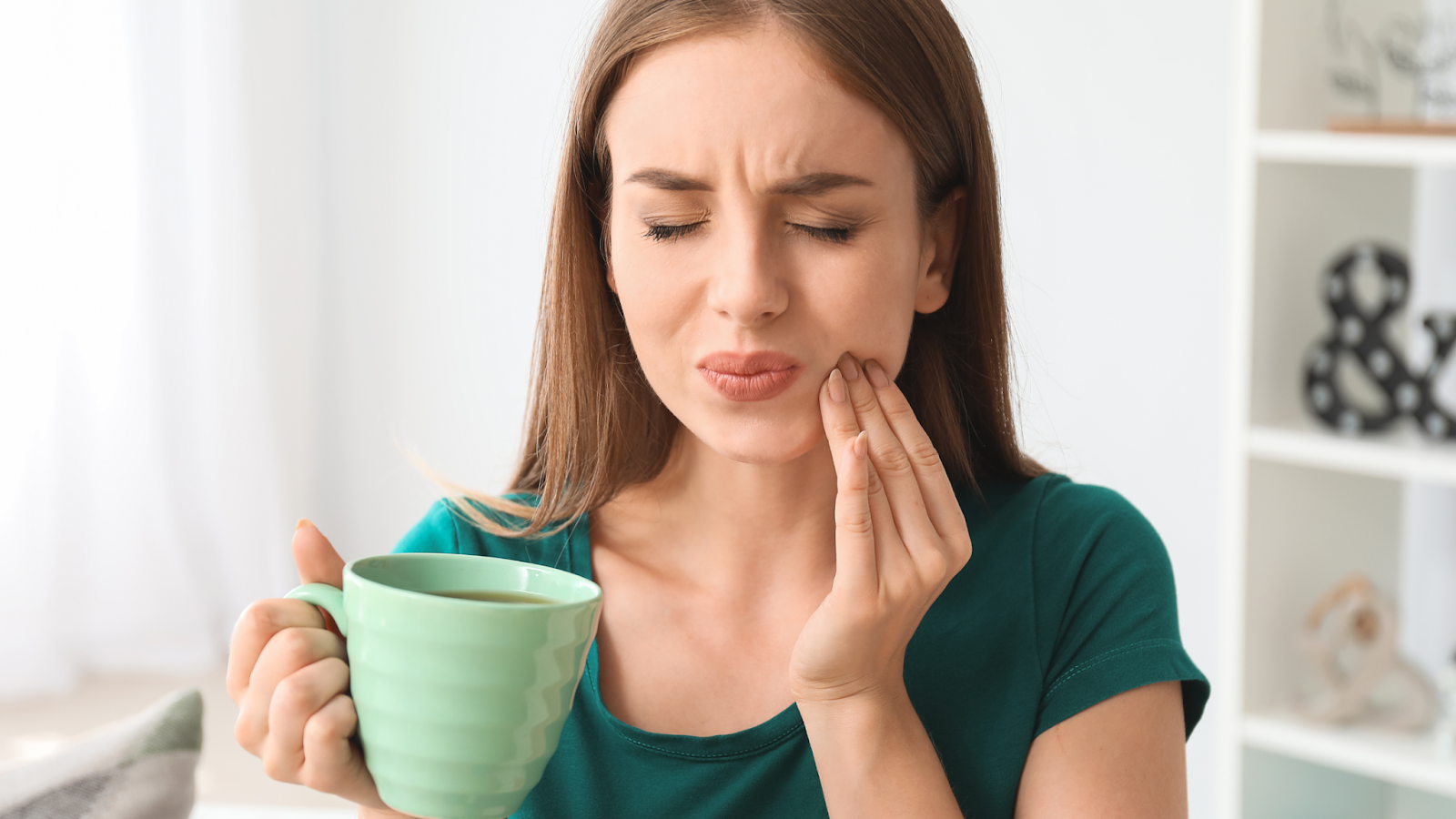 Woman with tooth pain after teeth whitening, holding a cup.