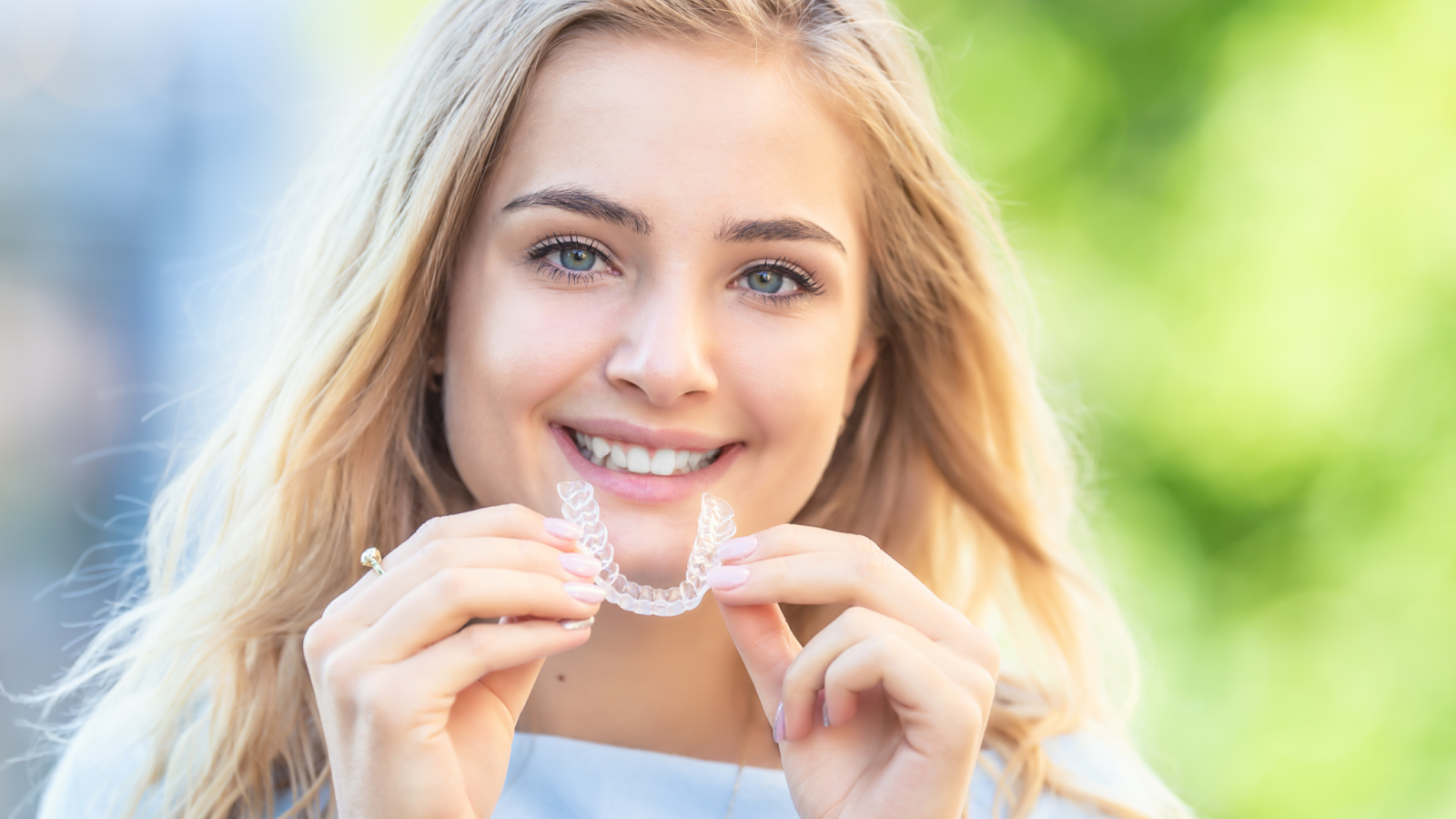 Smiling young woman holding Invisalign clear aligners, demonstrating the ease and comfort of the treatment.